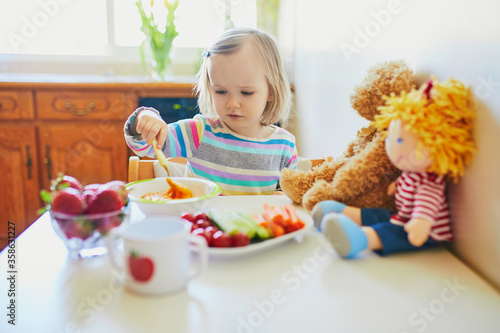 Adorable toddler girl eating fresh fruits and vegetables for lunch