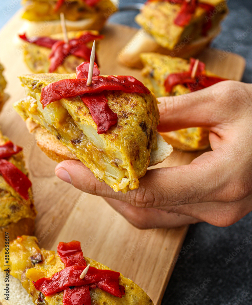 Spanish tortilla pintxo on a wooden board. Potato omelette on bread as a basque canape on sharing board. Party food. Spanish tortilla pintxo on a wooden board. Potato omelette on bread as a basque canape on sharing board. Party food.