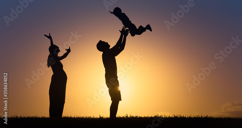 Happy family outdoors lifestyle silhouette. Father throwing up son in the air with happy pregnant mother cheering then on. 
