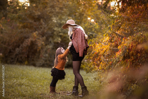 Young pregnant woman with long blond hair in hat playing with her little daughter at the autumn park. Copy space. photo