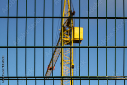 Yellow construction crane on construction site with fence in foreground and lots of blue sky