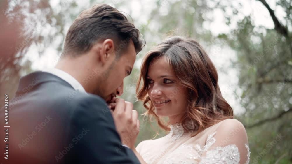 Couple in love from the first sight, emotional dating of handsome man and pretty woman in the garden. Happy man smiling and kissing girlfriend's hand with tenderness. Emotions of love between male and