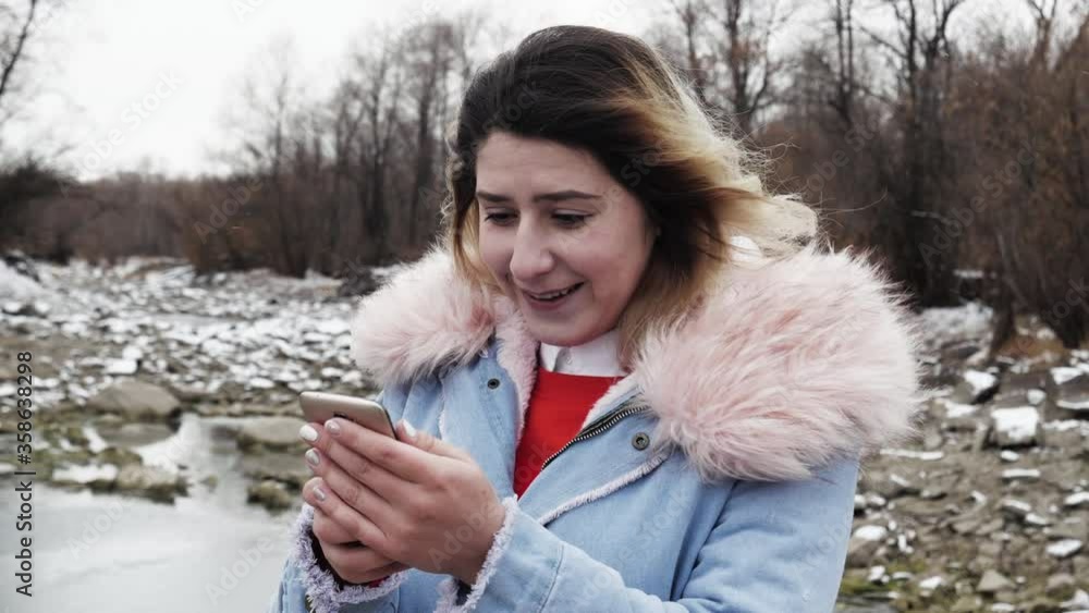 Attractive woman typing text message on phone close up in winter forest valley 4K. Girl read and write mobile in northern valley. Person type texting message with frosty north wind and reading answer. Attractive woman typing text message on phone close up in winter forest valley 4K. Girl read and write mobile in northern valley. Person type texting message with frosty north wind and reading answer.