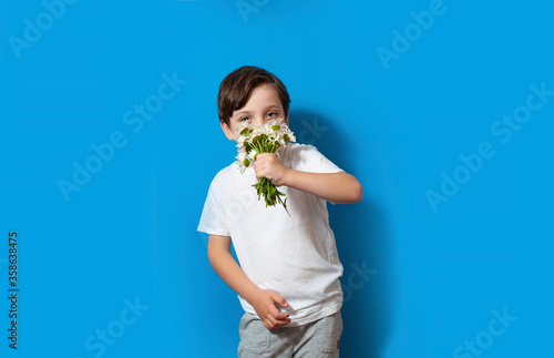 Happy beautiful kid boy holds flower bouquet on the yellow background. Children love nature and happy nature modern life © Olga Krivokoneva