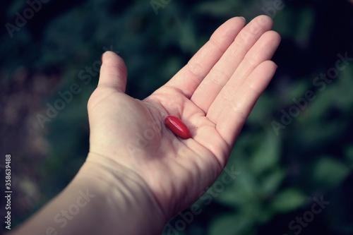 Close up of woman hand with red pill on green background © Maelia Rouch