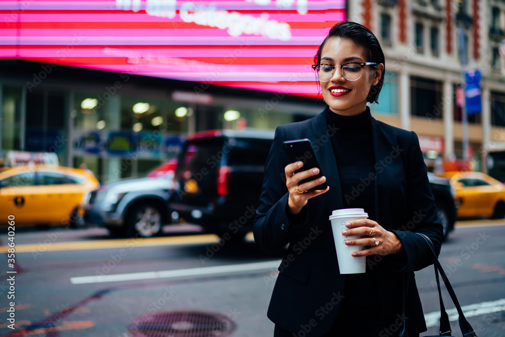 Successful female manager in trendy eyewear chatting online while waiting for taxi on avenue in new york, prosperous businesswoman in formal wear holding coffee to go cup and checking mail outdoors. Successful female manager in trendy eyewear chatting online while waiting for taxi on avenue in new york, prosperous businesswoman in formal wear holding coffee to go cup and checking mail outdoors.