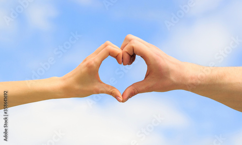 Heart from hands on a sky background. Love, friendship concept. Girl and male hand in heart form love blue sky. Female and man hands in the form of heart against the sky. Closeup © Yevhen