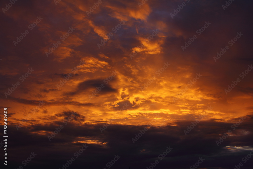 Dark blue orange colored windy dramatic sunset sky with sun rays illuminated stormy clouds on a summer evening, beautiful cloudscape, texture for background and wallpaper