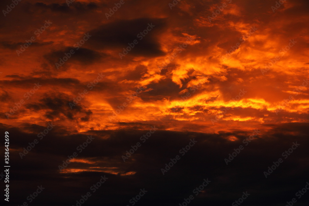 Heavy red black colorful dramatic storm clouds on sunset with sun rays illuminated  sky on a summer evening, beautiful cloudscape view, scenic texture for background and wallpaper