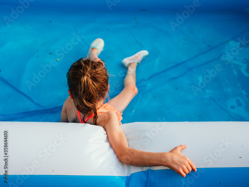 Fototapeta Young girl sits at the edge of a blowup pool on a warm summer night at sunset