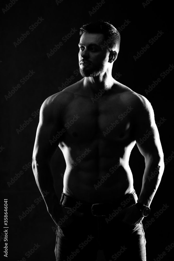 Fototapeta premium Strong athletic man fitness model. Male showing six pack abs. Isolated on dark background. Black and white photo.