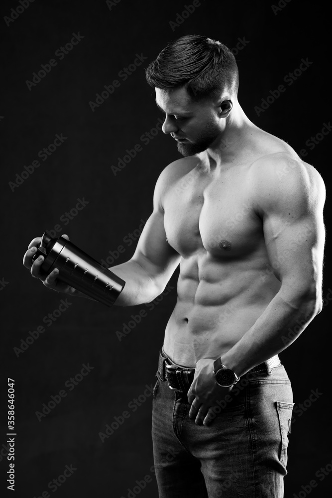Very muscular sporty guy holding protein drink. Man with naked torso. Athletic body. Sport and sport nutrition concept. Black and white photo. Very muscular sporty guy holding protein drink. Man with naked torso. Athletic body. Sport and sport nutrition concept. Black and white photo.