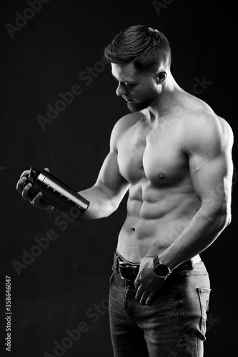 Very muscular sporty guy holding protein drink. Man with naked torso. Athletic body. Sport and sport nutrition concept. Black and white photo.