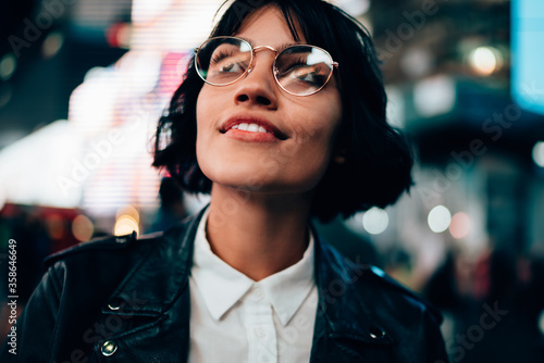 Obraz na plátně Fascinated pretty hipster girl in stylish eyeglasses amazed with night New York city walking in urban setting