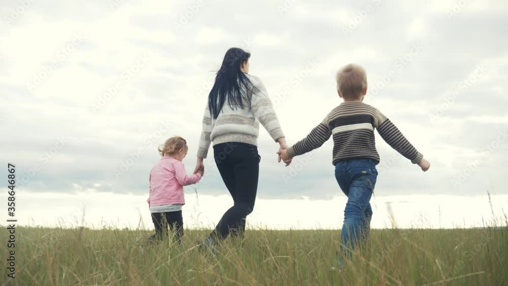 happy family. mom and little children walk in the park teamwork outdoors holding hands. woman and little boy and girl walk lifestyle on a green field at sunset happy family. mom and little children walk in the park teamwork outdoors holding hands. woman and little boy and girl walk lifestyle on a green field at sunset