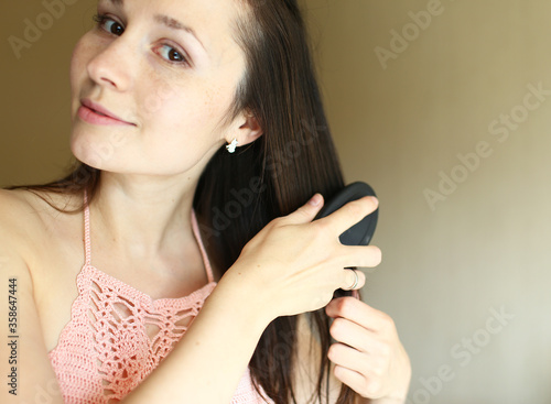 Young white brunette girl caring for hair. Girl puts oil and combes her hair