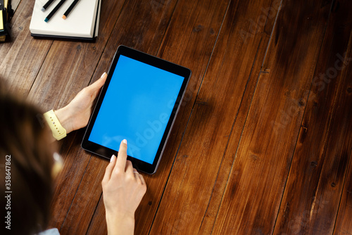 Mockup image of a woman using digital tablet with blank screen on wooden table. Close up photo of female hands holding device vertically