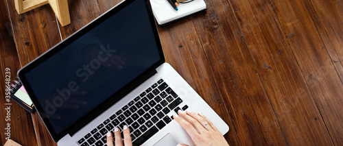 Mockup image of a woman using laptop with blank screen on wooden table