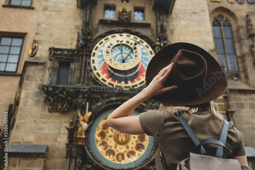 Blonde girl with hat and backback near famous clock in Prague, Czech Republic