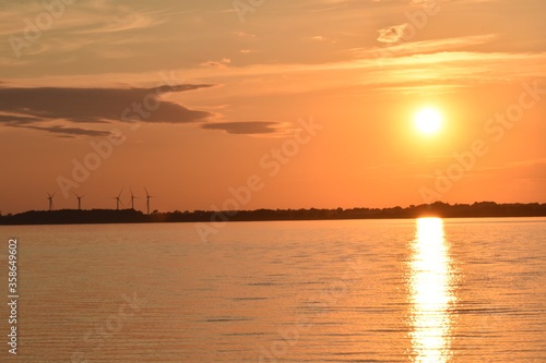 Wind turbines in the Eckernfoerde Bay  in Northern Germany. The setting sun paint the sky and the water of the Baltic Sea with shades of orange and gold.