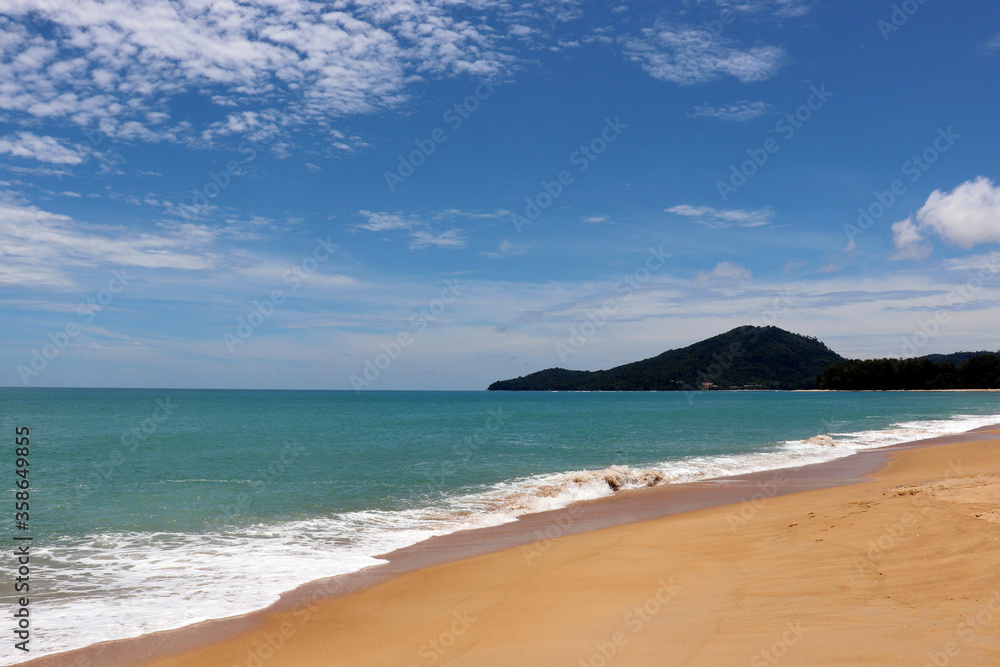 Tropical sandy beach with a frothy wave, scenic view to empty sea coast with yellow sand, azure water and forest. Picturesque seascape with blue sky and white clouds