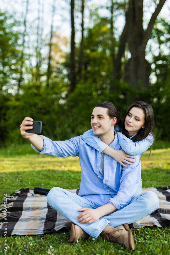 Loved young couple using mobile phone taking a selfie in the park Loved young couple using mobile phone taking a selfie in the park