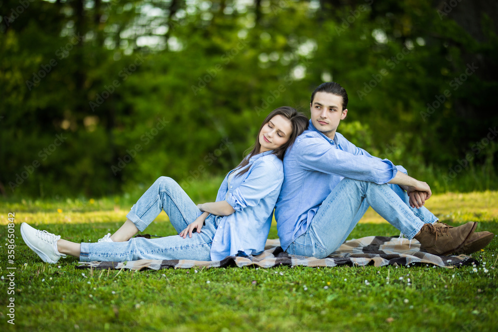 Young Couple sitting in the garden on the blanket back to back and girl is sad