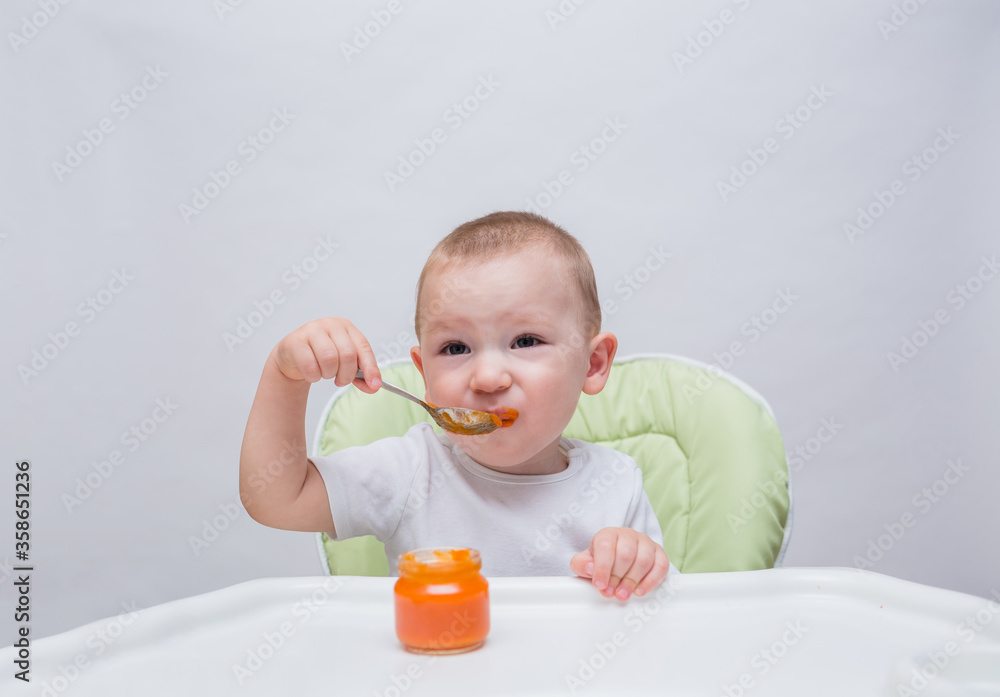 A small boy grimaces at a spoonful of mashed carrots at a table on a white background A small boy grimaces at a spoonful of mashed carrots at a table on a white background
