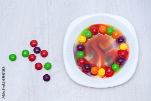 Science experiment for kids. Circle of colored candies on white plate.