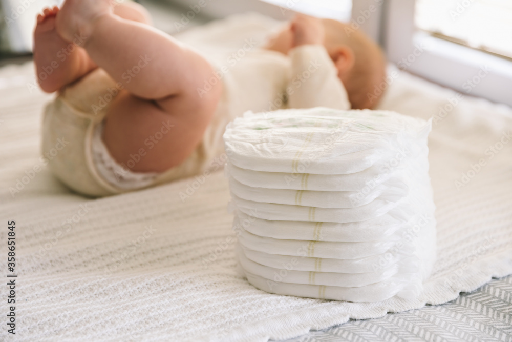 A baby in a diaper at the age of two months and a stack of diapers. How
