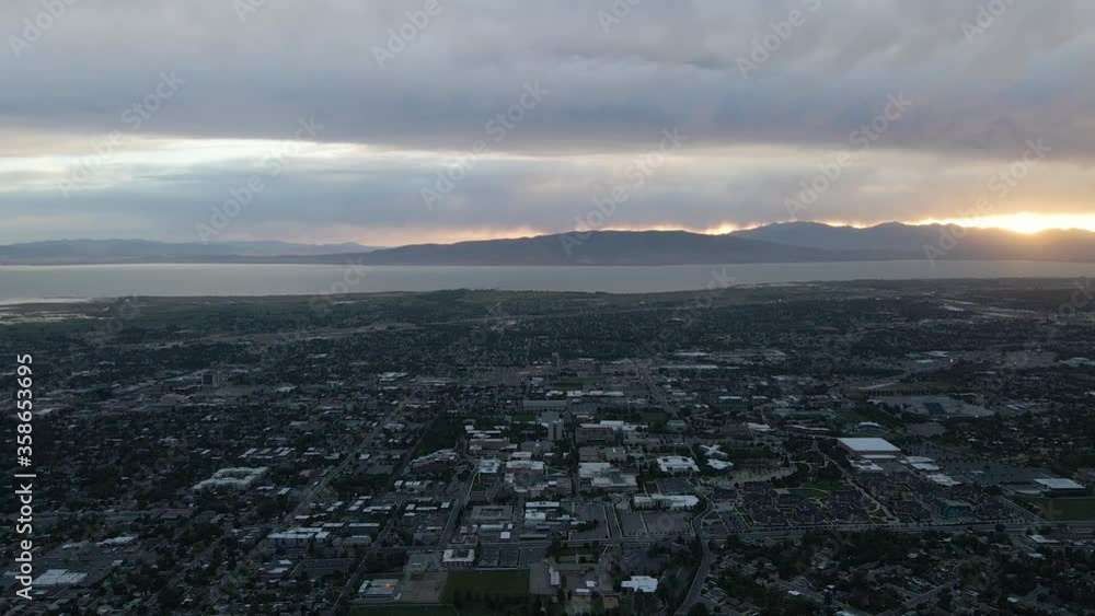 Overhead flight above downtown city skyline with water view and sunset above mountain range on cloudy day, circle aerial Overhead flight above downtown city skyline with water view and sunset above mountain range on cloudy day, circle aerial