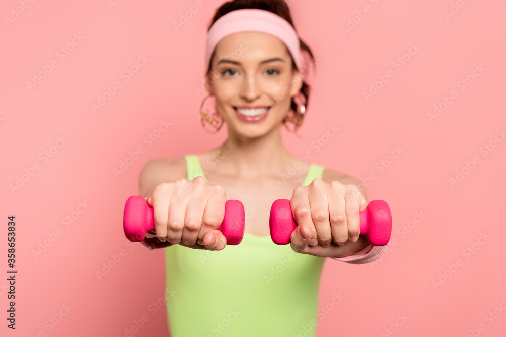 selective focus of happy sportswoman exercising with dumbbells isolated on pink selective focus of happy sportswoman exercising with dumbbells isolated on pink