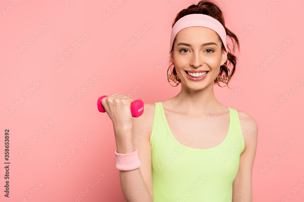cheerful sportswoman exercising with dumbbell on pink cheerful sportswoman exercising with dumbbell on pink
