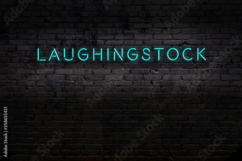 Night view of neon sign on brick wall with inscription laughingstock photo