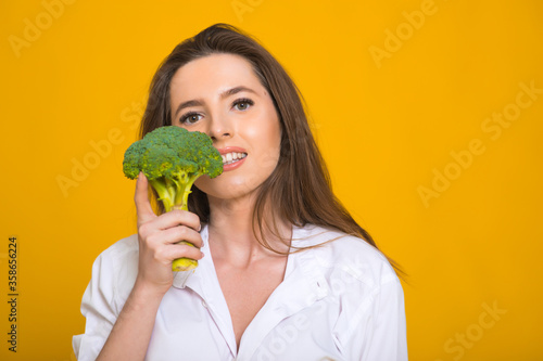 Detox diet concept. Woman holds green broccoli sprouts for healthy nutrition on yellow background, panorama, copy space
