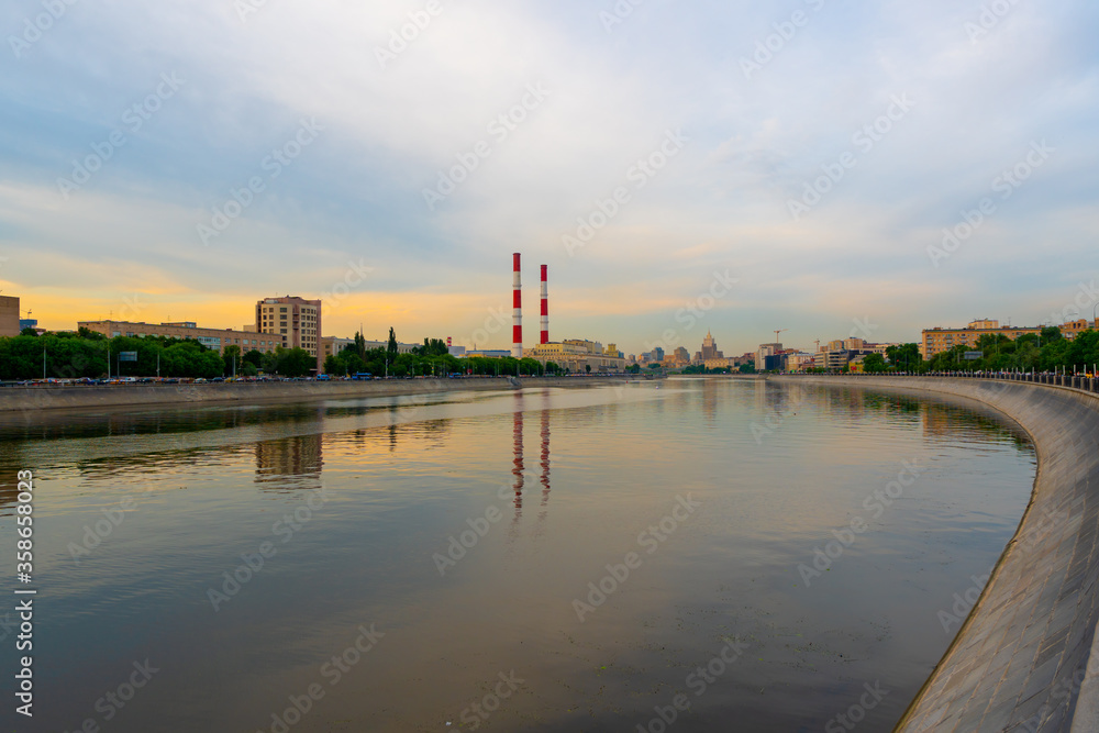 Sunset at Moscow river, amazing reflections on the water. Pipes of a thermal power plant with white and red stripes. Sunset at Moscow river, amazing reflections on the water. Pipes of a thermal power plant with white and red stripes.