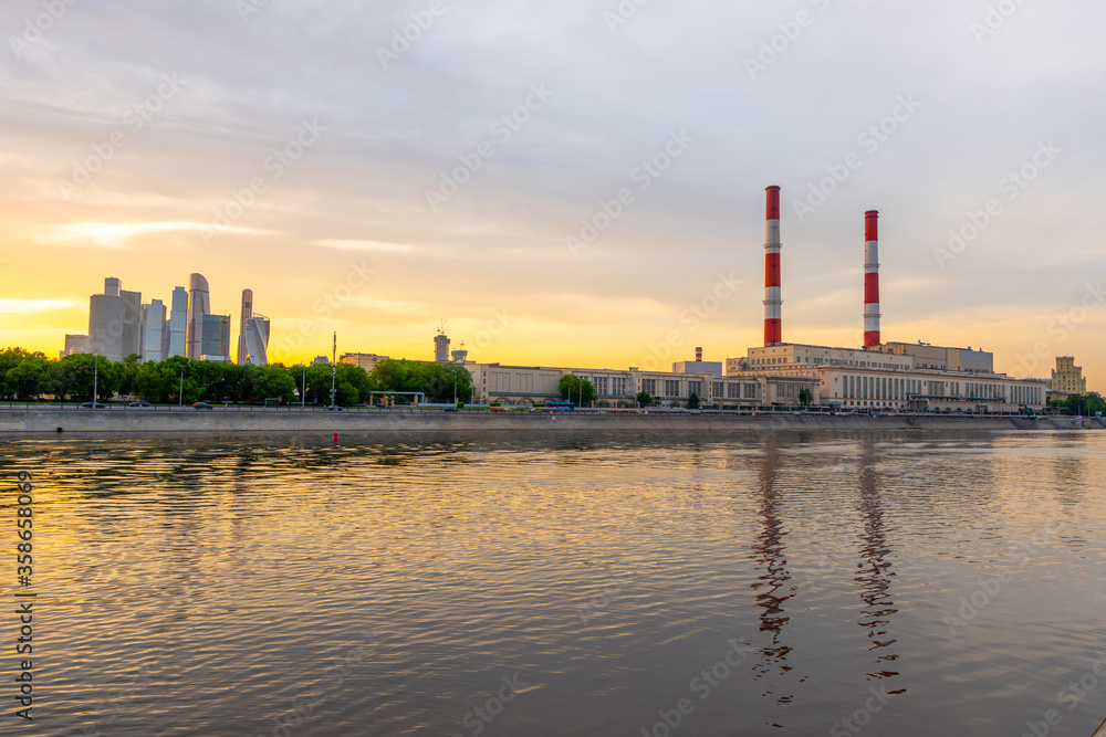 Naklejka premium Sunset at Moscow river, amazing reflections on the water. Pipes of a thermal power plant with white and red stripes. 