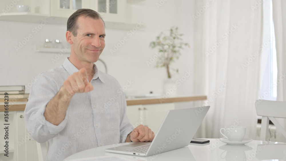 Cheerful Middle Aged Man with Laptop Pointing with Finger