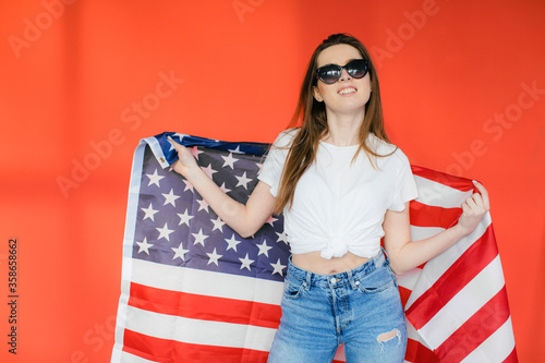 Patriotic holiday. Happy young woman with American flag on red background. USA celebrate 4th of July. © ALEXSTUDIO