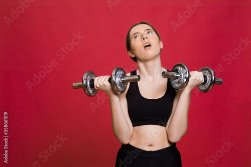 Sporty woman jumping with dumbbells. Photo of active woman in sportswear on red background. Dynamic movement. Sport and healthy lifestyle