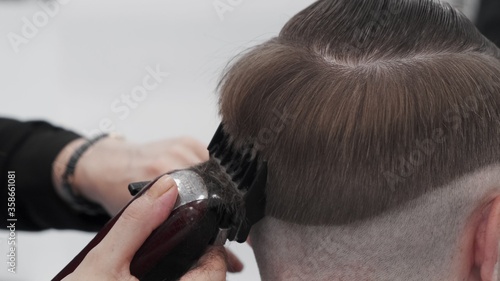 Cutting man hair with trimmer in salon. Close up head of guy with trendy haircut