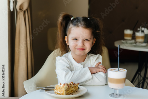 A cute little girl is sitting in a cafe and looking at a cake and cocoa close-up. Diet and proper nutrition