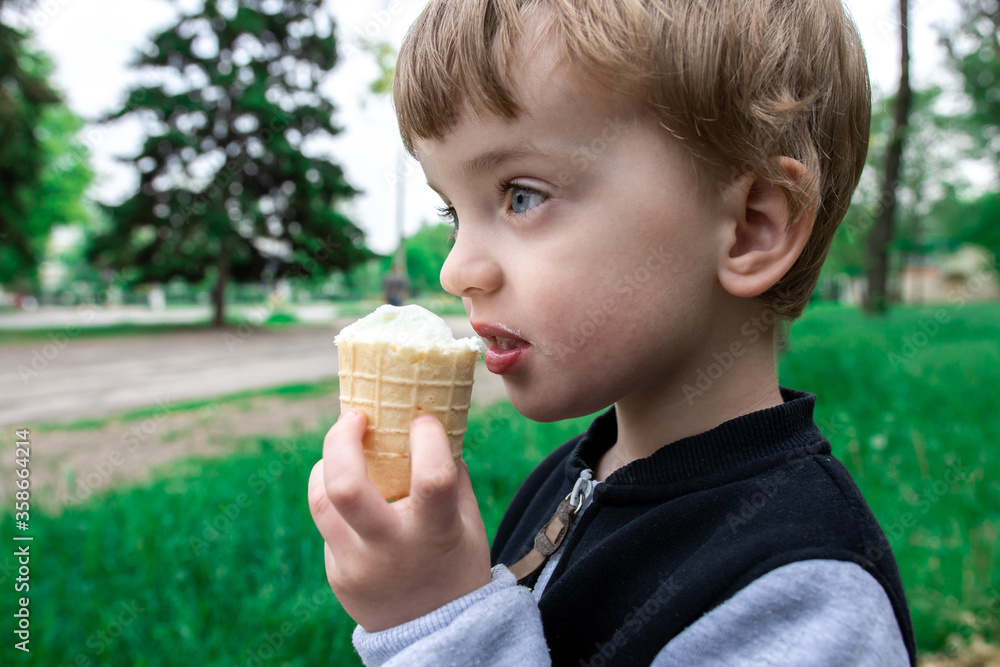 three year old boy eating ice cream in a waffle cup in a park. summer walks with your favorite food. junk food. close-up three year old boy eating ice cream in a waffle cup in a park. summer walks with your favorite food. junk food. close-up