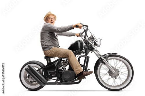 Excited elderly man riding a custom chopper motorbile and looking at the camera