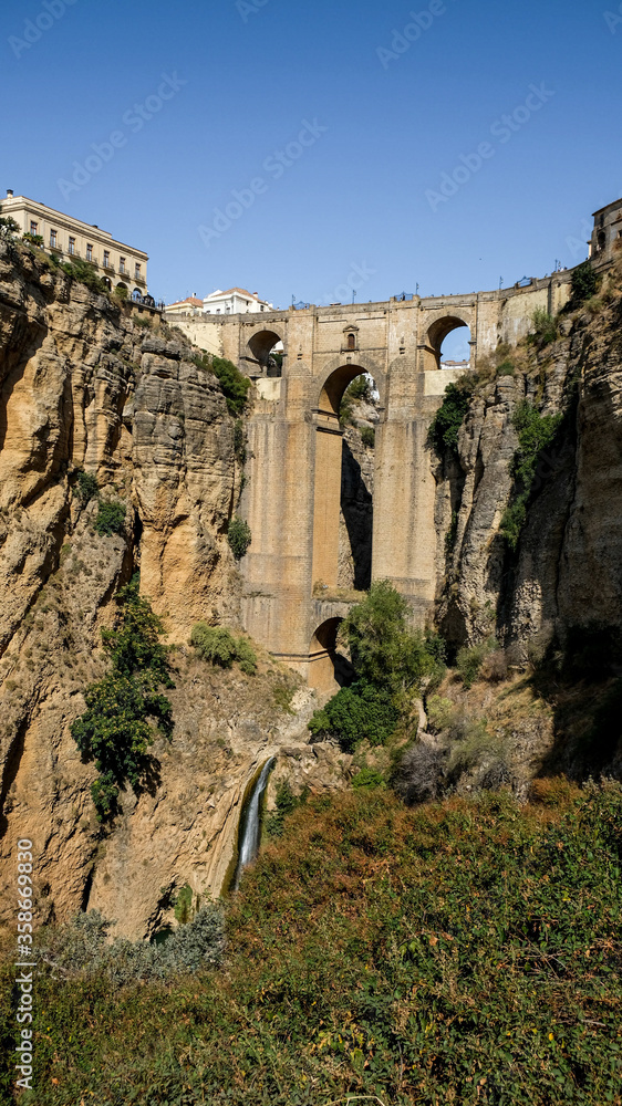 Puente Nuevo famous new bridge with archs in the heart of old village Ronda in Andalusia, Spain. Touristic landmark on a sunny day with buildings in the background. View from below.