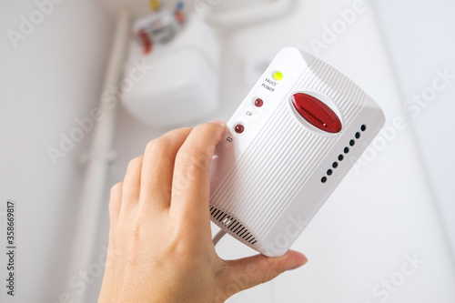 Typical gas sensor in Europe. White gas detector device in hand to prevent gas leaks and provide safety at home. Smoke detecting alarm in the European kitchen. Gas flow meter in the background at home