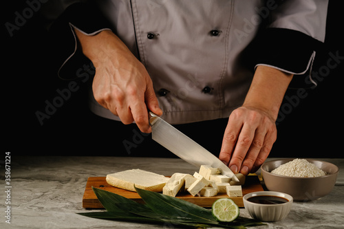 Fresh tofu pieces on bamboo leaves, on a wooden board ginger and lime.On a black background.Space for text.tofu in the hands of the cook