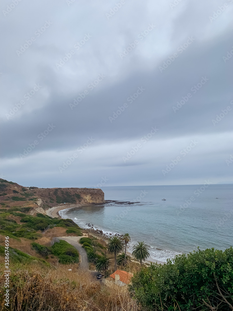 a gloomy overcast day overlooking a a earthy cliff at the edge of the coast with calm waters and shores