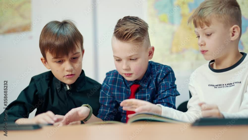 Cute boys study at school. Schoolchildren reading a book together while sitting in the classroom. Primary education at school. Cute boys study at school. Schoolchildren reading a book together while sitting in the classroom. Primary education at school.