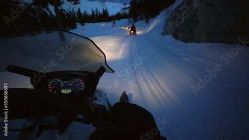 Slow motion shot of snowmobiles on snow by trees and rocks at night - Whistler, British Columbia photo